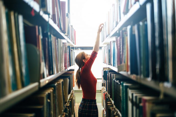 Eine Studierende nimmt ein Buch aus dem Regal einer Bibliothek