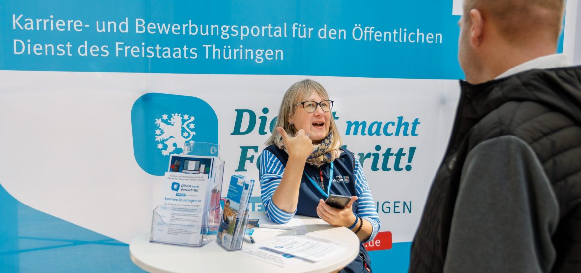 Frau erklärt Mann das Karriereportal für den Öffentlichen Dienst des Freistaats Thüringen am Messestand